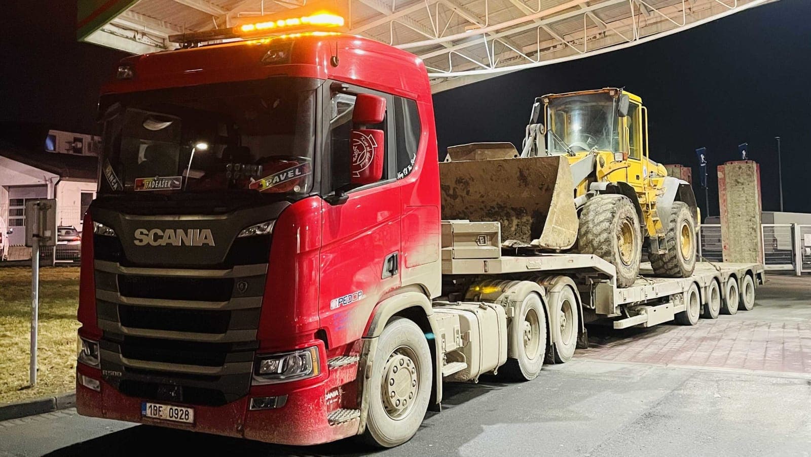 Červený tahač Scania PEDOP s vícenápravovým podvalníkem, na kterém je naložený kolový nakladač