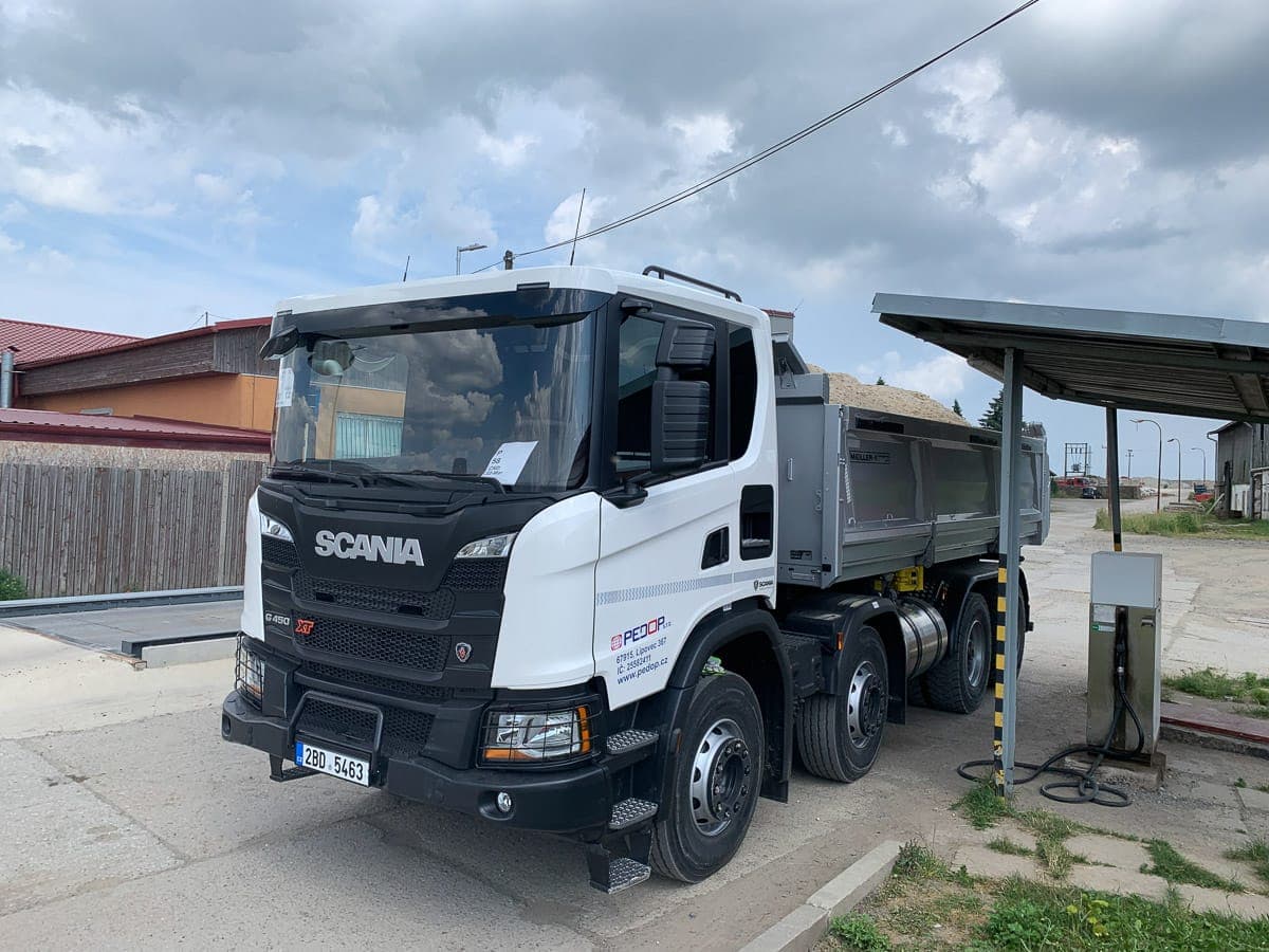 Bílý čtyřnápravový sklápěč Scania XT PEDOP naložený pískem v areálu